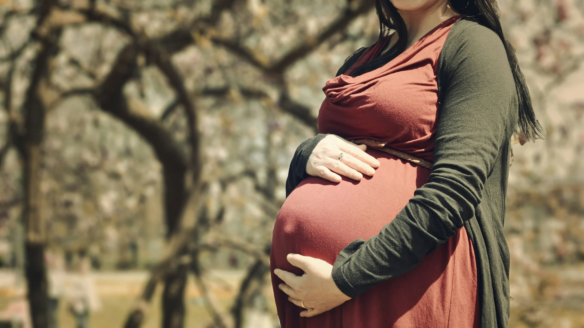 Schwangere Frau hält liebevoll ihren Babybauch im Freien